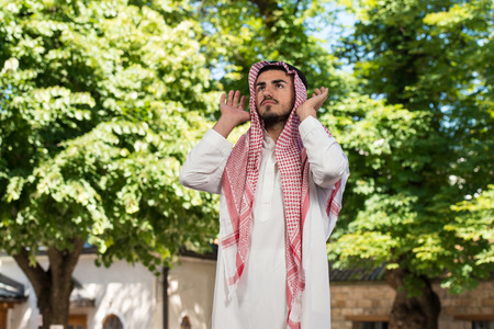 Young Muslim Man Making Traditional Prayer To God While Wearing A Traditional Cap Dishdashaの写真素材
