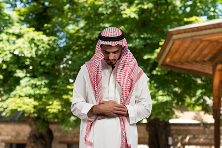 Young Muslim Man Making Traditional Prayer To God While Wearing A Traditional Cap Dishdashaの写真素材