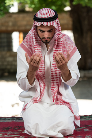 Young Muslim Man Making Traditional Prayer To God While Wearing A Traditional Cap Dishdashaの写真素材