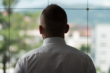 Young Businessman Looking Out Office Window Pondering Futureの写真素材