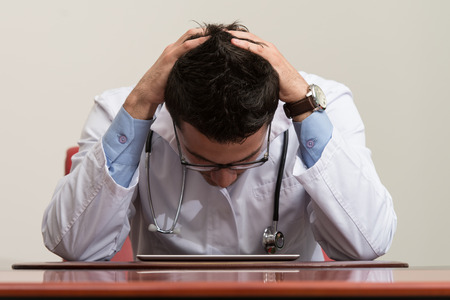Stressed Out Doctor With Hands Clasped Sitting At Table In Conference Roomの写真素材