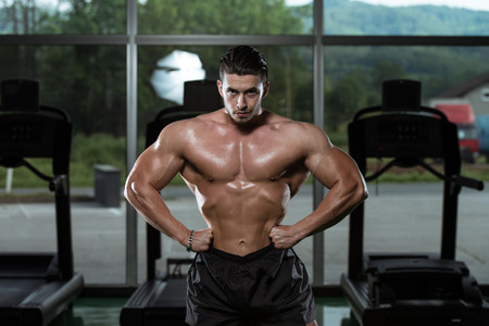 Serious Man Bodybuilder Standing In The Gym And Flexing Musclesの写真素材