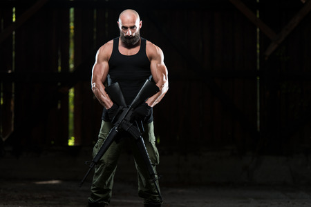 Action Hero Muscled Man Holding Machine Gun - Standing In Abandoned Building Wearing Green Pantsの写真素材