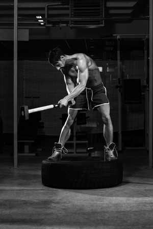 Athletic Man Hits Tire - Workout At Gym With Hammer And Tractor Tireの写真素材