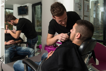Handsome Young Hairdresser Giving A New Haircut To Male Customer At Parlorの写真素材