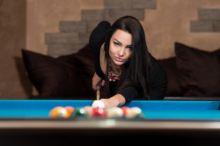 Young Woman Playing Billiards Lined Up To Shoot Easy Winning Shotの写真素材