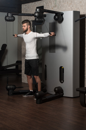 Handsome Man Is Working On His Shoulders With Cable Crossover In A Modern Gymの写真素材