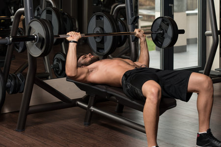 Handsome Man Is Working Out Chest With Barbell In A Modern Gym