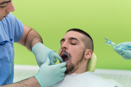 Closeup Of Male Dentist Examining Mid Adult Patient's Mouth In Clinic