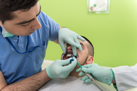Closeup Of Male Dentist Examining Mid Adult Patient's Mouth In Clinicの写真素材
