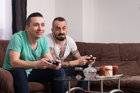 Two Young Gamers Sitting Together On Sofa And Playing Video Games At Homeの写真素材