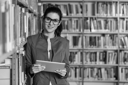 In The Library - Pretty Female Student With Tablet And Books Working In A High School - University Library - Shallow Depth Of Fieldの写真素材