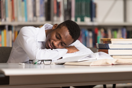 Sleeping African Student Sitting And Leaning On Pile Of Books In College - Shallow Depth Of Fieldの写真素材