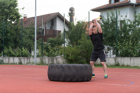 Young Man Hits Tire - Workout Outdoors With Hammer And Tractor Tireの写真素材