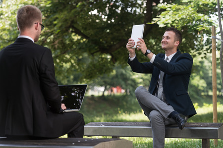 Happy Business Men Using Tablet Pc Outside On A Park Benchの写真素材