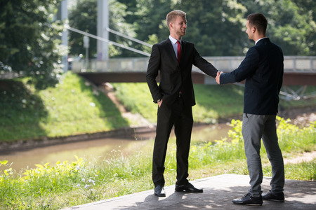 Happy Businessmen Shaking Hands While Standing Outdoors In Parkの写真素材