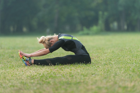 Young Woman Stretching Before Running In Wooded Forest Area - Training And Exercising For Trail Run Marathon Endurance - Fitness Healthy Lifestyle Conceptの写真素材
