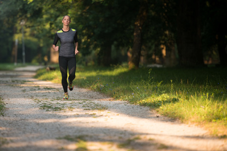 Young Woman Running In Wooded Forest Area - Training And Exercising For Trail Run Marathon Endurance - Fitness Healthy Lifestyle Conceptの写真素材