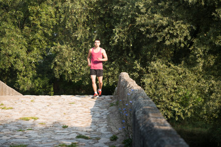 Young Man Running In Wooded Forest Area - Training And Exercising For Trail Run Marathon Endurance -...