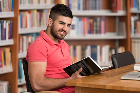 In The Library - Handsome Arabic Male Student With Laptop And Books Working In A High School - University Library - Shallow Depth Of Fieldの写真素材