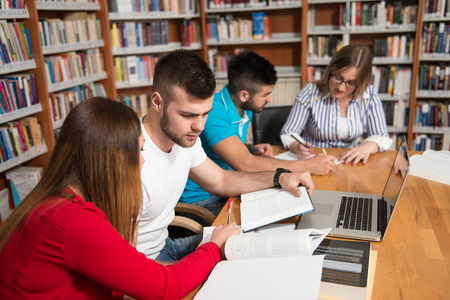 In The Library - Handsome Group Of Students With Laptop And Books Working In A High School - University Library - Shallow Depth Of Fieldの写真素材