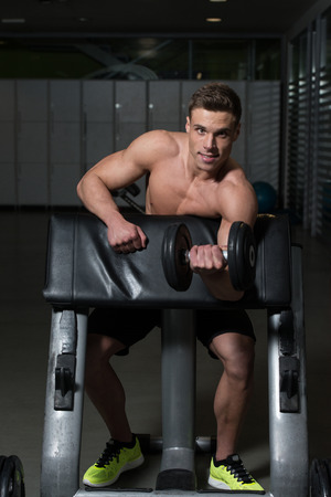 Muscular Young Man Doing Heavy Weight Exercise For Biceps With Dumbbell In Gymの写真素材