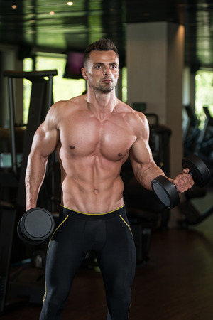 Muscular Young Man Doing Heavy Weight Exercise For Biceps With Dumbbells In Modern Fitness Center Gymの写真素材