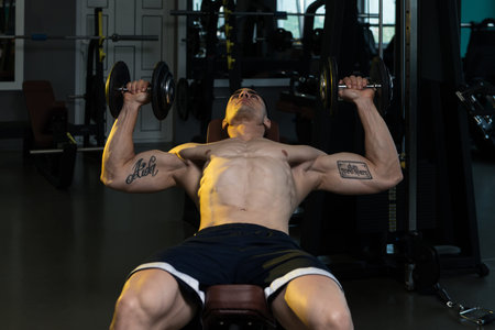 Muscular Man Doing Exercise For Chest With Dumbbells In A Gym