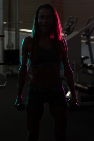 Silhouette Woman Standing Strong In The Gym And Flexing Musclesの写真素材