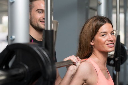 Personal Trainer Showing Young Woman How To Train Barbell Squats Exercise In A Gymの写真素材
