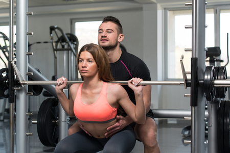 Personal Trainer Showing Young Woman How To Train Barbell Squats Exercise In A Health And Fitness Conceptの写真素材