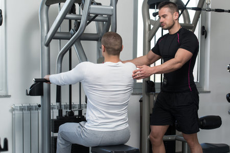 Personal Trainer Showing Young Man How To Train Back On Machine In The Gym