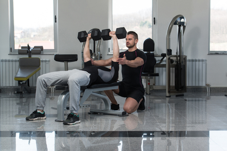 Personal Trainer Showing Young Man How To Train Chest Exercise With Dumbbells In A Health And Fitness Conceptの写真素材