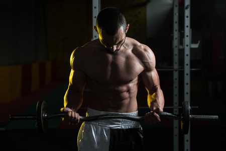 Young Athlete In The Gym Performing Biceps Curls With A Barbellの写真素材