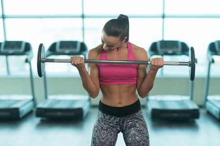 Young Woman Exercising Biceps With Barbell In The Gym And Flexing Muscles - Muscular Athletic Bodybuilder Fitness Modelの写真素材