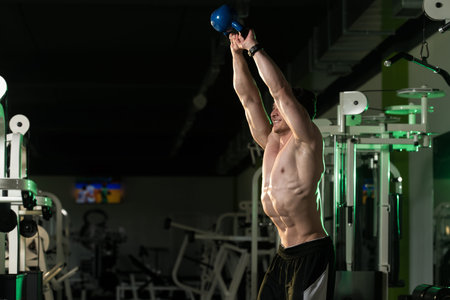 Young Man Working Out With Kettle Bell In A Dark Gym - Bodybuilder Doing Heavy Weight Exercise With...