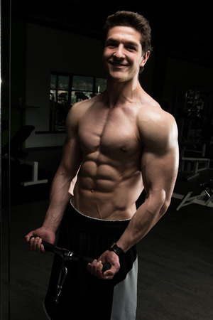 Young Muscular Fitness Bodybuilder Doing Heavy Weight Exercise For Biceps On Machine With Cable In The Gymの写真素材