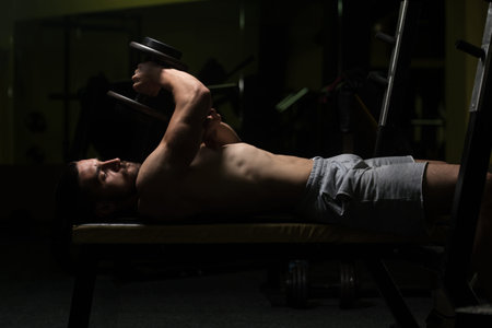 Young Muscular Man Doing Heavy Weight Exercise For Triceps With Dumbbell In Gym