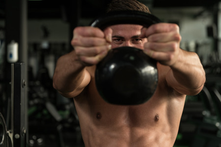 Young Man Working Out With Kettle Bell In A Gym - Bodybuilder Doing Heavy Weight Exercise With Kettle-bellの写真素材