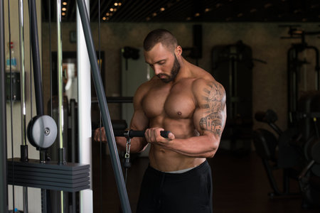 Big Tattooed Man In The Gym Is Exercising Biceps On Machine - Muscular Athletic Bodybuilder Model...