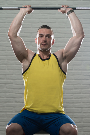 Young Man Working Out Triceps With Barbell On White Bricks Background With Copyspaceの写真素材