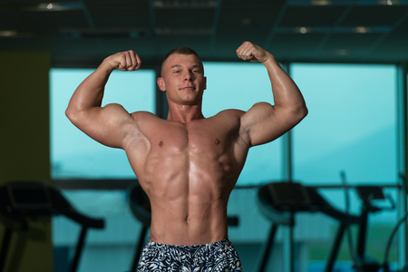 Young Man Standing Strong In The Gym And Flexing Muscles - Muscular Athletic Bodybuilder Fitness Model Posing After Exercisesの写真素材