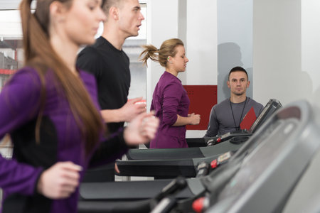 Group Of Young People Running On Treadmills In Gym Or Fitness Club While Personal Trainer Measure...
