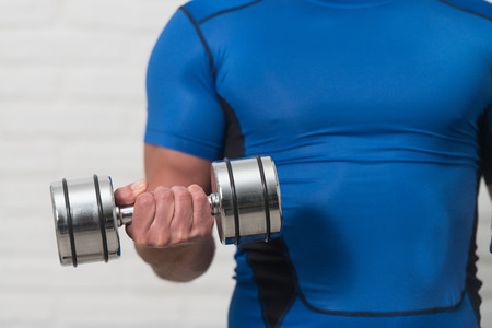 Close Up Personal Trainer Working Out Biceps With Dumbbells On White Bricks Background With Copyspace - Dumbbell Concentration Curlsの写真素材