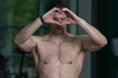 Portrait Of A Young Physically Fit Man Showing Heart With Hands - Muscular Athletic Bodybuilder Fitness Model Posing After Exercisesの写真素材