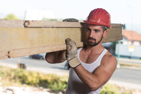 Smiling Carpenter Carrying A Large Wood Plank On His Shoulderの写真素材