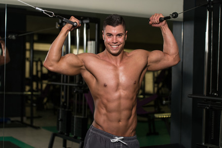 Young Man Is Working On His Biceps With Cable Crossover In A Modern Fitness Gymの写真素材