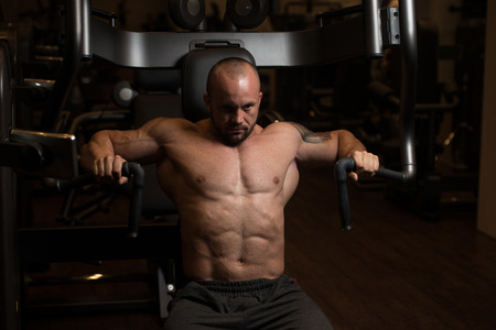 Big Man In The Gym Is Exercising Back On Machine - Muscular Athletic Bodybuilder Model Exercise In Fitness Centerの写真素材