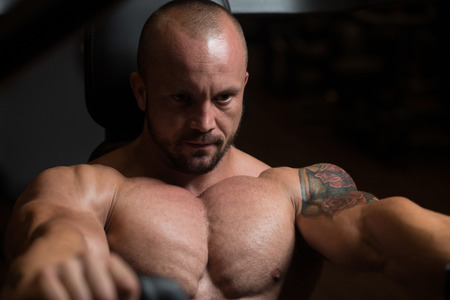 Big Man In The Gym Is Exercising Back On Machine - Muscular Athletic Bodybuilder Model Exercise In Fitness Centerの写真素材