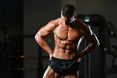 Healthy Man Standing Strong In The Gym And Flexing Muscles - Muscular Athletic Bodybuilder Fitness Model Posing After Exercisesの写真素材